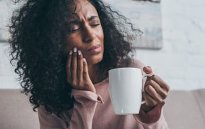 woman holding a cup in one hand and rubbing on her jaw in the other