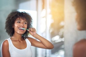 Black woman brushing teeth in the mirror